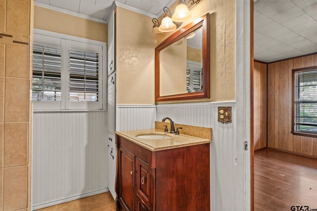 bathroom featuring wood-type flooring, vanity, wooden walls, and ornamental molding