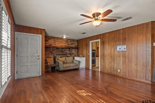 unfurnished room with wooden walls, wood-type flooring, ceiling fan, and a fireplace