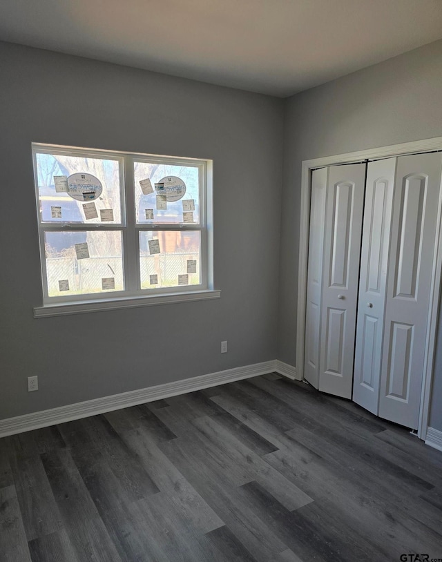 unfurnished bedroom featuring a closet, dark wood-style floors, and baseboards