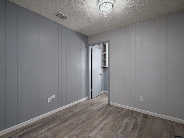 unfurnished room with wood walls, hardwood / wood-style flooring, and a textured ceiling