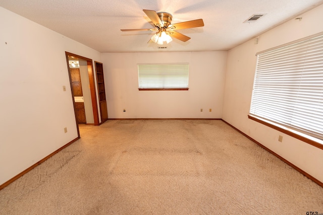 unfurnished room with ceiling fan, a textured ceiling, and light colored carpet