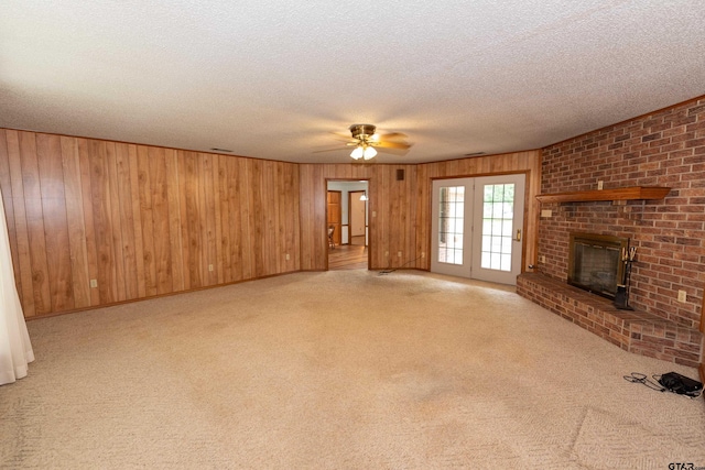 unfurnished living room with a textured ceiling, wood walls, light carpet, and ceiling fan