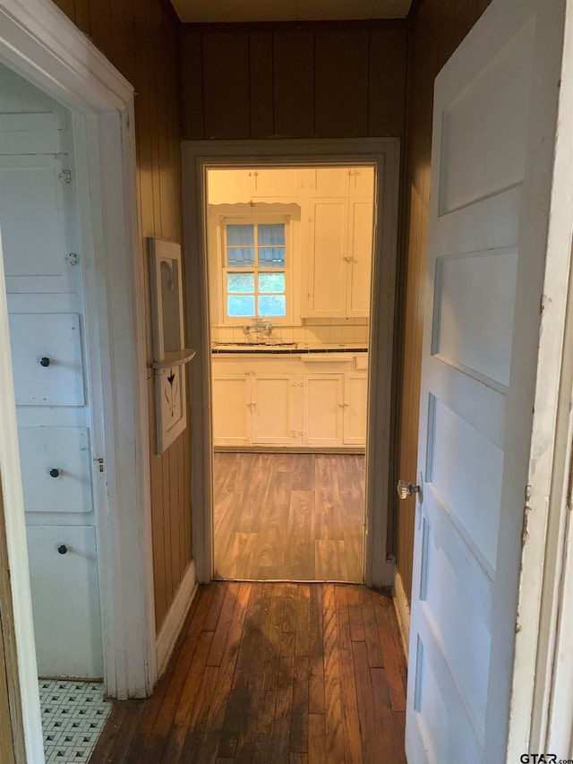 hall featuring dark hardwood / wood-style flooring, wooden walls, and sink