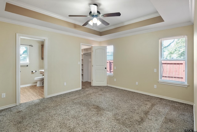 unfurnished bedroom with a walk in closet, ornamental molding, a tray ceiling, ceiling fan, and ensuite bathroom