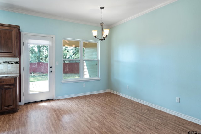 unfurnished dining area with light wood-type flooring, crown molding, and an inviting chandelier