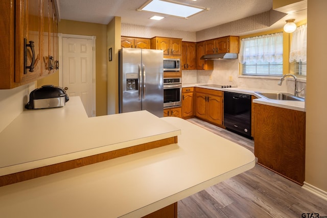 kitchen featuring sink, light hardwood / wood-style flooring, kitchen peninsula, decorative backsplash, and black appliances