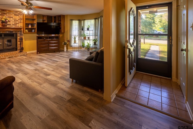 entrance foyer featuring hardwood / wood-style flooring, ceiling fan, and a brick fireplace