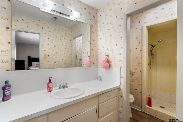 bathroom featuring hardwood / wood-style floors, vanity, toilet, and a tile shower