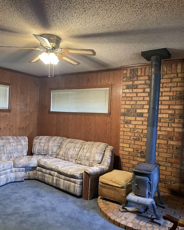 carpeted living room with a textured ceiling, ceiling fan, a wood stove, and wooden walls