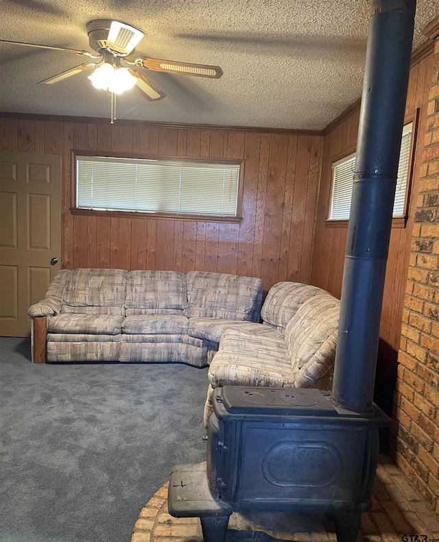 carpeted living room featuring ceiling fan, wood walls, a textured ceiling, and a wood stove