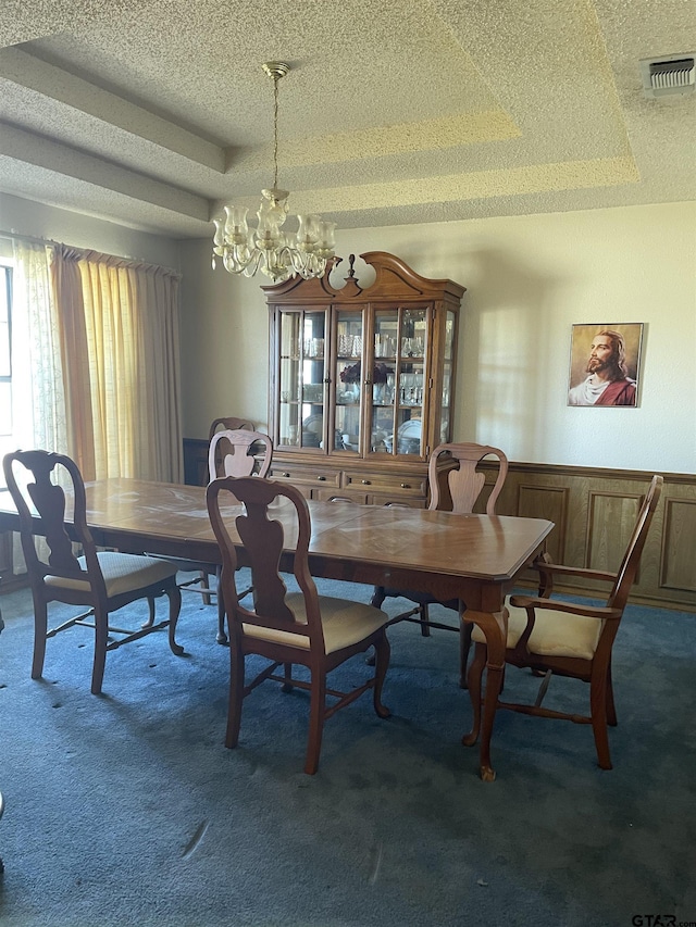 carpeted dining area with a textured ceiling, wooden walls, an inviting chandelier, and a tray ceiling