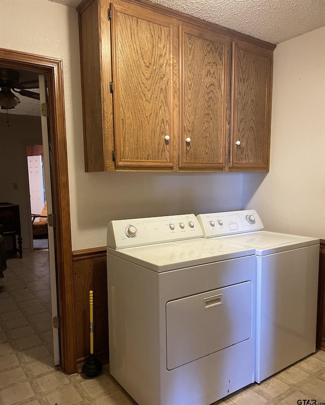 clothes washing area featuring a textured ceiling, cabinets, ceiling fan, washer and clothes dryer, and wood walls