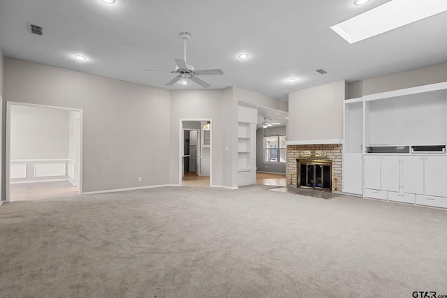 unfurnished living room featuring ceiling fan, a skylight, light carpet, and a brick fireplace