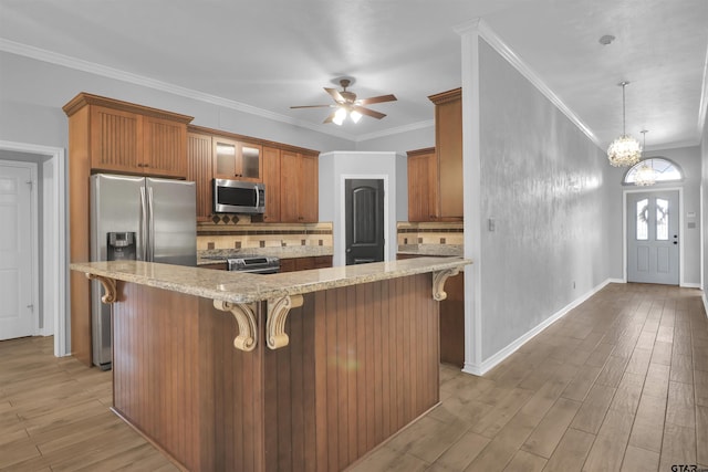 kitchen featuring backsplash, a breakfast bar, crown molding, stainless steel appliances, and ceiling fan with notable chandelier