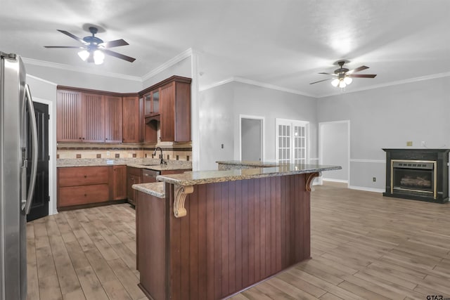 kitchen featuring kitchen peninsula, a kitchen bar, light stone countertops, and stainless steel refrigerator