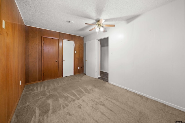 unfurnished bedroom with a textured ceiling, ceiling fan, dark carpet, and wood walls