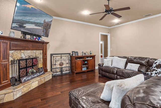 living room featuring ceiling fan, ornamental molding, dark hardwood / wood-style floors, and a stone fireplace