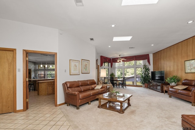 carpeted living room with a skylight, wood walls, and ceiling fan