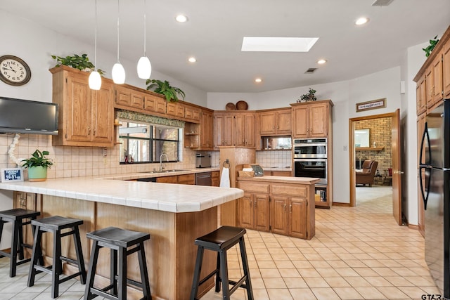 kitchen with tile countertops, a breakfast bar area, a skylight, kitchen peninsula, and stainless steel appliances