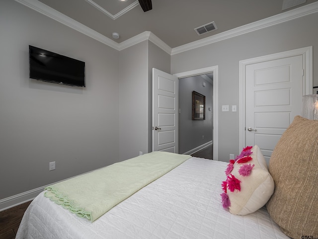 bedroom with baseboards, visible vents, crown molding, and wood finished floors