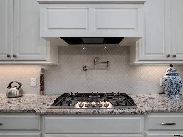 kitchen with white cabinetry, range hood, backsplash, light stone countertops, and stainless steel gas stovetop