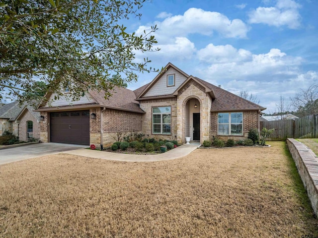 french provincial home featuring a shingled roof, concrete driveway, brick siding, and fence