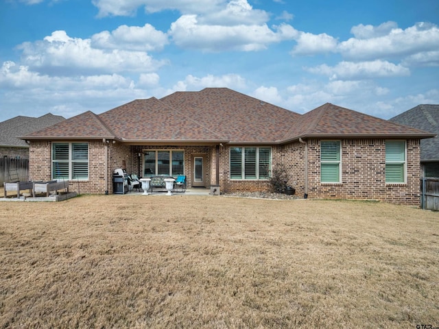 back of house featuring a yard, a patio, brick siding, and roof with shingles