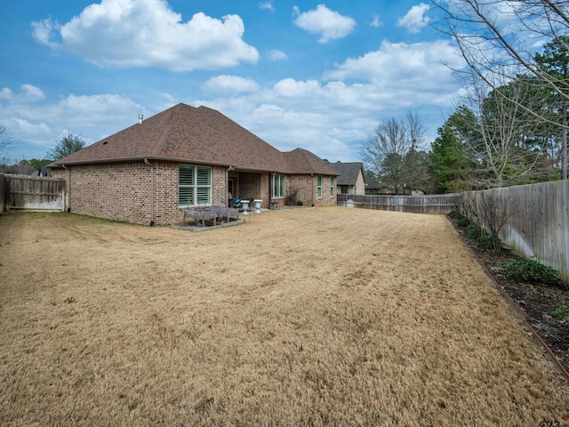 rear view of house featuring a yard, a fenced backyard, roof with shingles, and brick siding