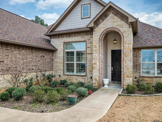 property entrance with stone siding, roof with shingles, and brick siding