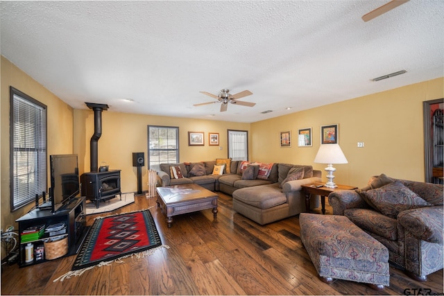 living room with a wood stove, a textured ceiling, visible vents, and dark wood-style flooring