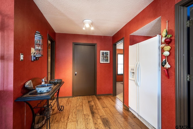 hall with light wood-type flooring and a textured ceiling