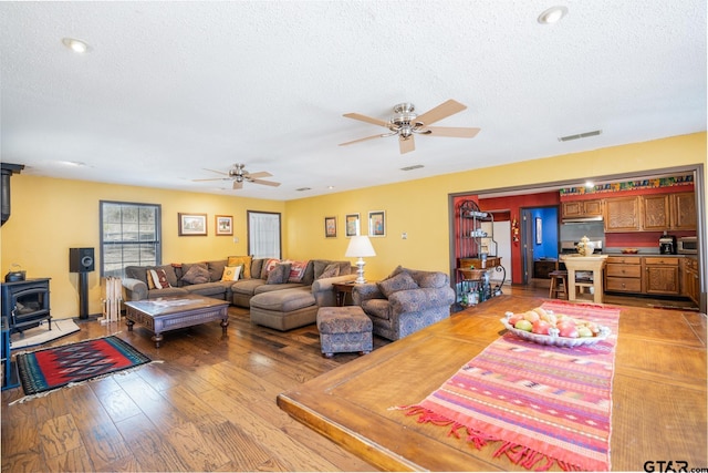 living room featuring a wood stove, a textured ceiling, visible vents, and wood finished floors