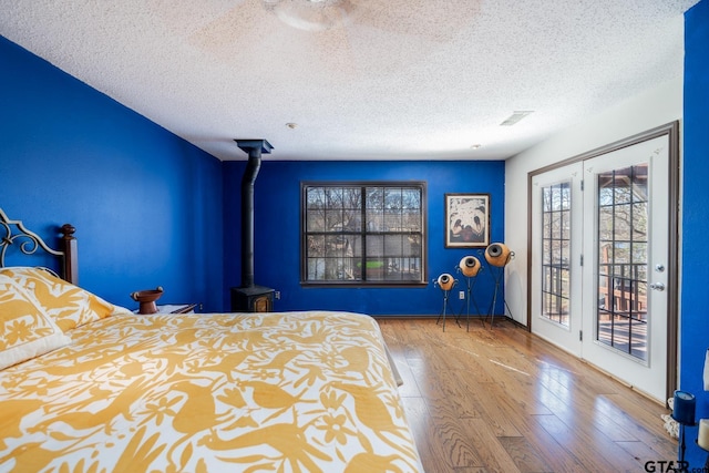 unfurnished bedroom with a textured ceiling, wood finished floors, visible vents, access to outside, and a wood stove