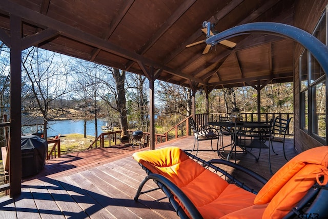 wooden deck with a water view, a ceiling fan, a gazebo, grilling area, and outdoor dining space