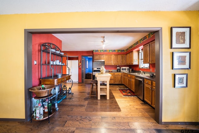 kitchen featuring dark countertops, appliances with stainless steel finishes, a sink, wood finished floors, and baseboards