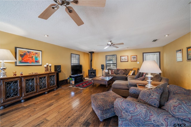 living room with a wood stove, ceiling fan, a textured ceiling, and wood finished floors