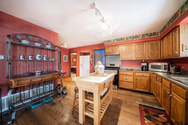 kitchen featuring appliances with stainless steel finishes, brown cabinets, dark wood finished floors, and under cabinet range hood