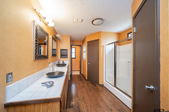 full bathroom with visible vents, a sink, a shower stall, and wood finished floors