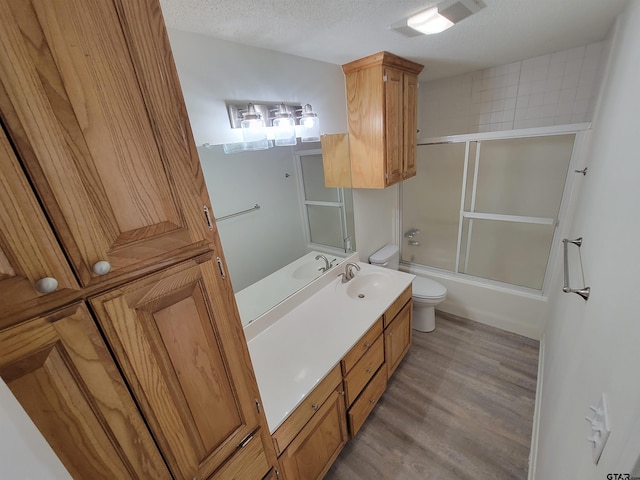 full bathroom featuring hardwood / wood-style floors, bath / shower combo with glass door, a textured ceiling, toilet, and vanity