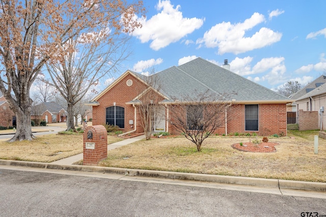 view of front of house featuring brick siding, roof with shingles, a front yard, and fence