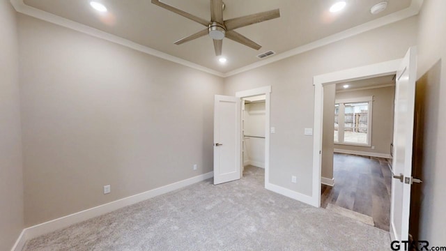 unfurnished bedroom featuring ceiling fan, light colored carpet, ornamental molding, and a spacious closet