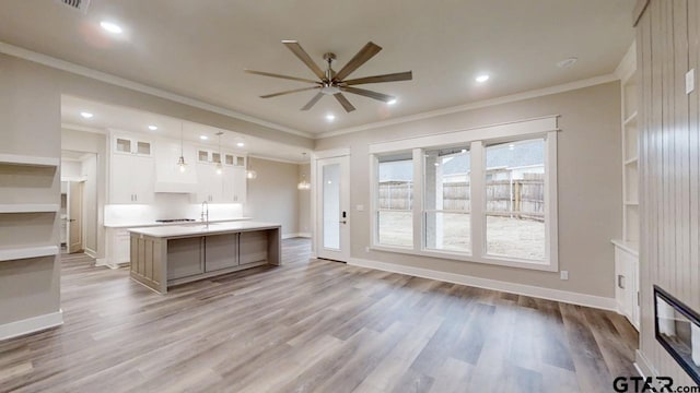 kitchen with light hardwood / wood-style flooring, pendant lighting, a fireplace, a kitchen island with sink, and white cabinets