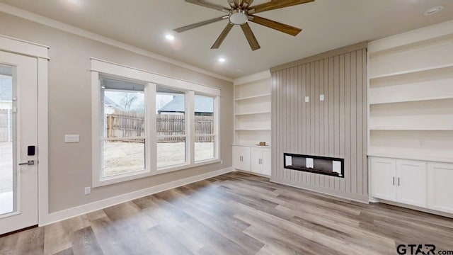 unfurnished living room featuring crown molding, built in features, ceiling fan, light hardwood / wood-style floors, and a large fireplace