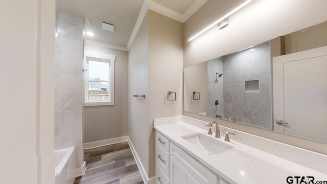 bathroom with vanity, wood-type flooring, crown molding, and tiled shower / bath