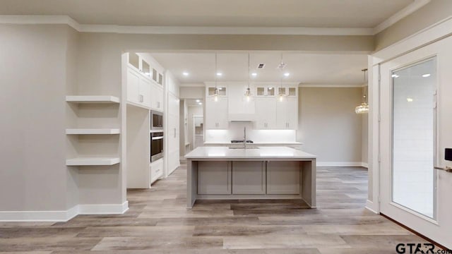 kitchen with white cabinetry, wall oven, an island with sink, and hanging light fixtures