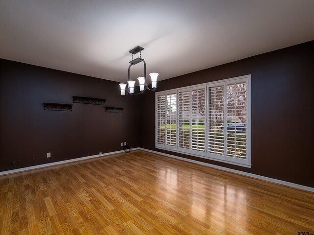 spare room featuring wood-type flooring and an inviting chandelier