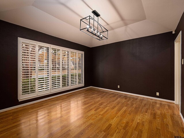 unfurnished dining area with a tray ceiling, wood-type flooring, a wealth of natural light, and an inviting chandelier