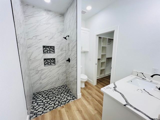 bathroom featuring hardwood / wood-style floors, vanity, toilet, and a tile shower