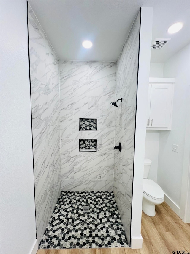 bathroom featuring toilet, hardwood / wood-style floors, and tiled shower