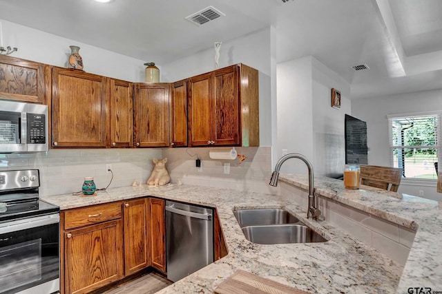 kitchen featuring sink, light stone counters, light wood-type flooring, appliances with stainless steel finishes, and decorative backsplash